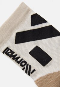 Calcetines de punto con una base beige y patrones geométricos en negro y crema, tejido texturizado y la marca "NORMATZ" en costura negra.