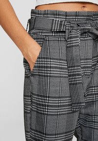 Černobílé kostkované kalhoty s uvázaným páskem a bočními kapsami, vyrobené z texturované tkaniny a s pevnějším střihem.