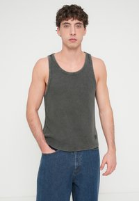 Σκούρο γκρι βαμβακερό αμάνικο τοπ με στρογγυλεμένο λαιμόκοψη και ραβδωτή υφή, συνδυασμένο με φαρδιά μπλε τζιν παντελόνια. Το μοντέλο στέκεται με τα χέρια στις τσέπες.