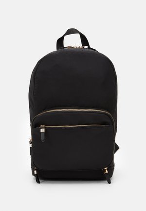 Černý nylonový batoh zaobleného tvaru, s přední kapsou na zip a zlatými kovovými detaily. Obsahuje nastavitelné popruhy a horní ucho.