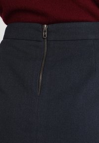 Gonna nera con zip laterale visibile, vestibilità sartoriale e tessuto testurizzato. Presenta un orlo pulito e dettagli di cucitura minimi.