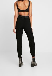 Zwarte cropped tanktop gecombineerd met hoge zwarte cargo broek met zijzakken en elastische manchetten, gedragen met grijze slangenhuid enkellaarsjes.