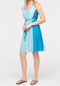 Robe sans manches avec un décolleté en V, présentant un dégradé de couleur allant du bleu clair au bleu foncé. Fabriquée en tissu léger, elle comprend un détail de taille nouée.