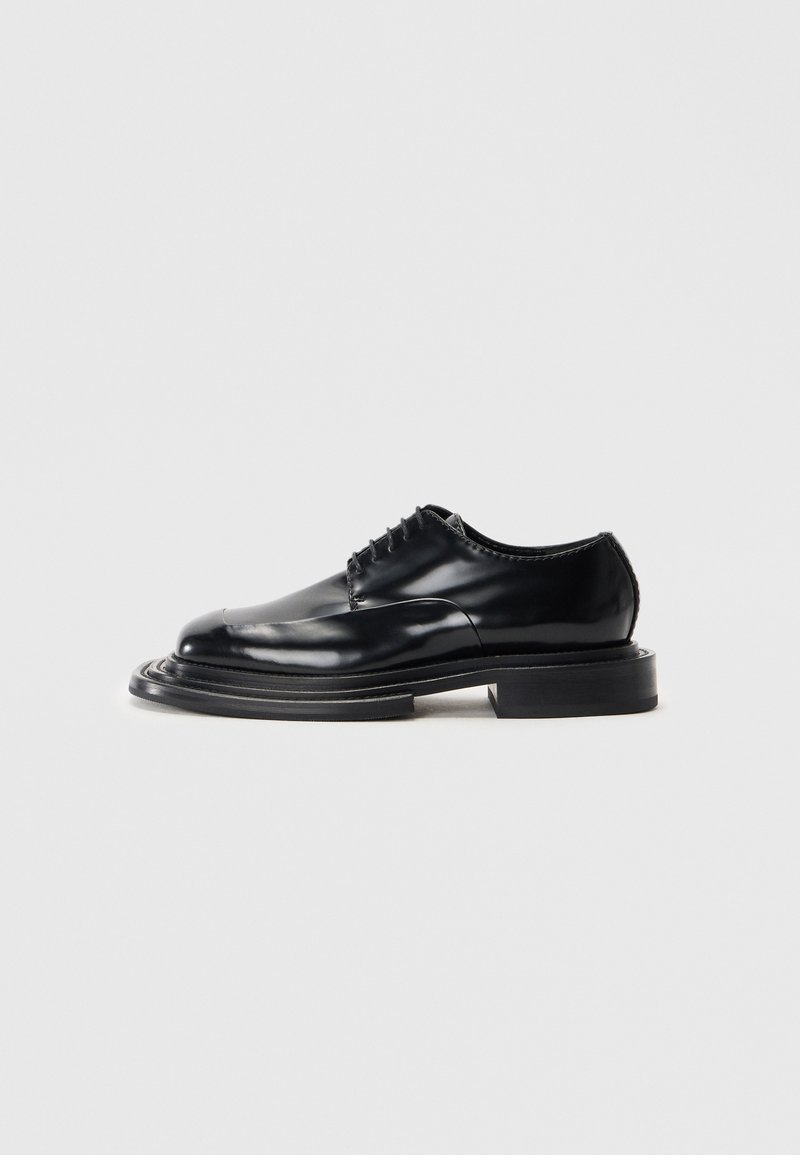 Scarpa in pelle nera con finitura lucida, punta arrotondata, lacci e suola spessa e piatta. Presenta un design stratificato e scolpito.