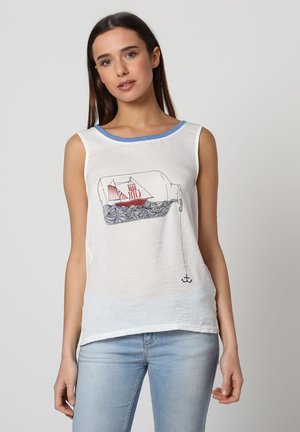 Mujer con camiseta sin mangas blanca con ribete azul y gráfico de un barco en una botella flotando sobre olas con una línea de ancla, combinada con jeans azul claro.