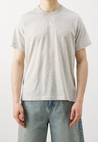 Šedé bavlněné tričko s krátkým rukávem, kulatým výstřihem a malým bílým logem uprostřed. Uvolněný střih s hladkou texturou.