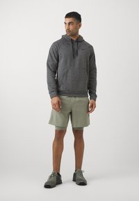 Grå hættejakke med en frontlomme, sammen med lysegrønne shorts. Modellen har grå sportssko på og står foran en ensfarvet baggrund.