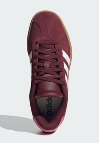 Maroon velur tenisice s bijelim prugama, gumeni potplat od gume, i podstavljeni jezik. Sadrže smeđe vezice i sivi uložak s "adidas" logotipom.