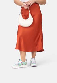 Bunt gefärbte Sportsneaker aus weichem Material mit weißer Sohle und dezentem Leopardenmuster, kombiniert mit einem seidigen orangen Rock und einer weißen Handtasche.