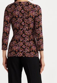 Blommig långärmad topp med svart bakgrund och mönster i rosa, orange och lila; mjukt tyg med en figurnära silhuett.