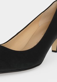 Escarpin en daim noir à talon moyen, bout arrondi et doublure intérieure beige, présenté de face et de profil sur un fond uni.