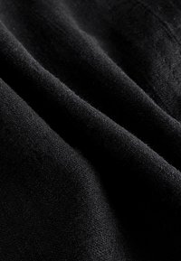 Zbliżenie na miękkie czarne fałdy tkaniny pokazujące teksturę i drobne szczegóły dzianiny.