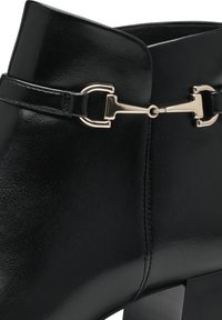 Black leather ankle boot featuring a sleek design, square heel, and a gold-tone buckle accent on a strap near the top. Smooth texture.