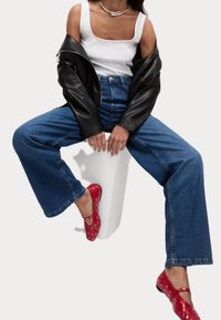 Svart läderjacka över en vit tanktop, kombinerad med vida jeans i blå denim och ballerinaskor med röda prickar.