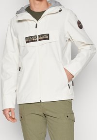 White, lightweight jacket with a gray hood, featuring a black logo patch on the chest, zippered side pockets, and a front zipper closure.