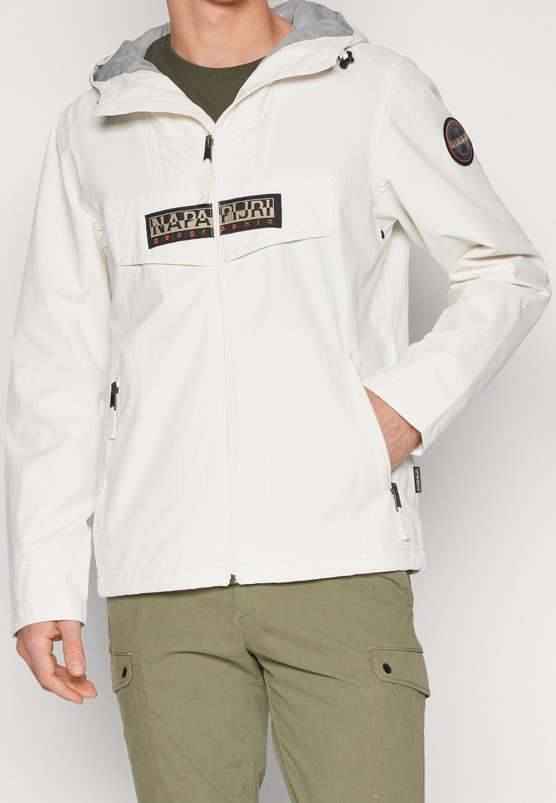 White, lightweight jacket with a gray hood, featuring a black logo patch on the chest, zippered side pockets, and a front zipper closure.