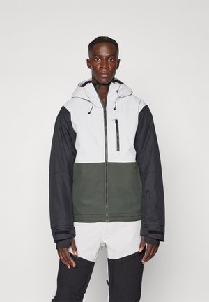Chaqueta con bloques de color en blanco, negro y verde oscuro; cuenta con capucha, cierre frontal y bolsillo en el pecho con cremallera. Tejido liso y duradero.
