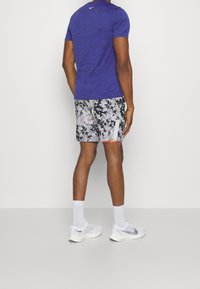 Mörklila tränings-T-shirt för herrar med korta ärmar, matchad med mönstrade grå shorts med svarta detaljer, vita strumpor och vita träningsskor.