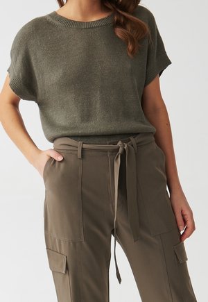 Mujer con un top de punto de manga corta en color oliva metido en pantalones cargo de talle alto en color oliva con cinturón anudado y bolsillos de parche.