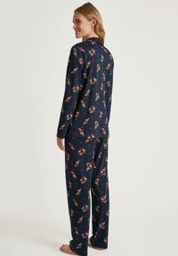Marineblaue Schlafanzugset aus weichem Stoff mit einem durchgehenden Muster von Rehen und Herzen. Lange Ärmel und locker sitzende Hosen, mit einem Kragen-Detail.