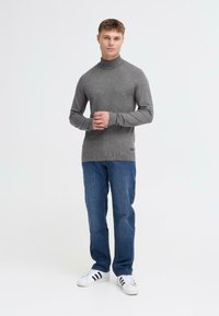 Grå turtleneck sweater i et blødt, ribbet stof; parret med blå jeans og hvide sneakers med sorte striber.