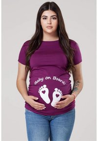 Lilla rasedus t-särk, millel on "Baby on Board" tekst ja valged jalajälje graafikad. Lühikesed varrukad, kehaümber käiv disain ja pehme materjal.