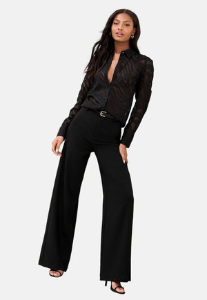 Black, sheer, long-sleeve blouse with a subtle animal pattern, paired with high-waisted, wide-leg black trousers and black heeled sandals.