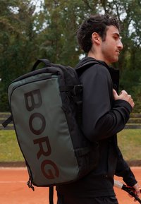 Zwarte en groene rugzak met groot "BORG" logo, van duurzaam materiaal, met gewatteerde schouderbanden en meerdere compartimenten, geschikt voor sportactiviteiten.