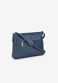 Bolso cruzado de cuero sintético azul con un compartimento con cremallera, correa ajustable y forma plana. Presenta un pequeño logo decorativo.
