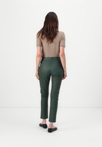 Brun kortärmad topp i kombination med snäva mörkgröna byxor med en slät yta. Modellen bär svarta ballerinaskor. Bakgrunden är helt vit.