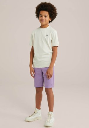 Lichtgroene T-shirt met een klein zwart logo, gecombineerd met lavendelkleurige shorts en witte hoge sneakers. Casual pasvorm met zachte stoffen.