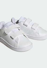 Białe dziecięce sneakersy z dwoma rzędami rzepów, perforowanymi bocznymi paskami, wyściółką wokół kostki i teksturowanymi gumowymi podeszwami na jednolitym tle.