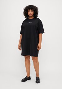Robe T-shirt noire oversize en coton doux. Caractérisée par des manches courtes et un petit motif brodé sur la poitrine.