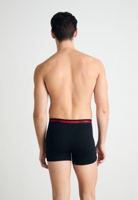 Boxer shorts noirs avec une ceinture logo rouge, design ajusté, texture lisse, et sans motifs ou accents supplémentaires.