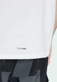 Hvid t-shirt med et "CLIMACOOL" logo i bunden, lavet af et glat stof med en afslappet pasform, parret med mørke mønstrede shorts.