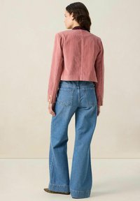Veste en velours côtelé rose raccourcie avec une finition texturée et des boutons dorés, associée à un jean bleu taille haute avec une coupe droite.