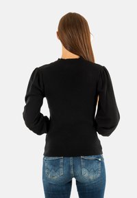 Maglione nero a coste con maniche lunghe a sbuffo e scollatura a zigzag, abbinato a jeans blu con un design distintivo sulle tasche posteriori.