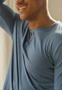 Blauw langemouw henley-shirt met een zachte textuur, voorzien van een knoopsluiting en een losse pasvorm die soepel over de schouder valt.
