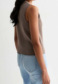 Brun ribbad ärmlös topp med en figurnära design, ihop med ljusblå högmidjade jeans, med bakfickor och mjuk textur.