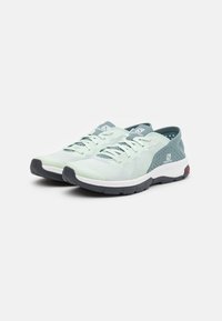 Light green athletic shoes with a mesh upper, grey accents, rounded toe, and textured rubber outsole. Features laces and logo detail.