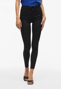 Pantalones vaqueros negros ajustados con cintura alta, tejido con un ligero estiramiento, sin adornos visibles y con una textura suave y elegante.