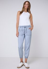 Pantalones jogger de color azul claro con puños elásticos y una cinturilla con cordón. Llevados con una camiseta sin mangas blanca y zapatillas blancas.