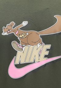 Gráfico de um canguru castanho com um canguru menor na sua barriga. Fundo de tecido verde com o swoosh rosa da Nike e texto "NIKE" em bege texturizado.