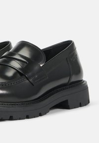 Mustad nahast loafers, millel on läikiv viimistlus, esiosa rihma detail, paks kummitald ja tugevdatud õmblused äärte ümber.