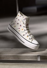 Tênis alto feitos de lona branca com bordados florais multicoloridos, apresentando cadarços brancos e uma sola de borracha preta.