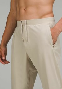 Ljusbeige träningsbyxor med en mjuk yta, elastisk midja, dragsko, sidofickor och en avslappnad passform.