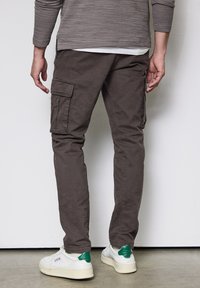 Bruna cargobyxor med sidofickor, tillverkade av bomull. Har en smal passform och bärs med vita sneakers och gröna detaljer. Slät textur.