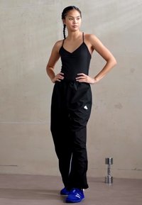 Black athletic tank top with thin straps, paired with black loose-fit pants featuring white accents, and blue athletic shoes.