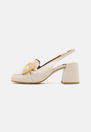 Beżowe, skórzane czółenka typu slingback z szerokim obcasem i dużą ozdobną klamrą z przodu.