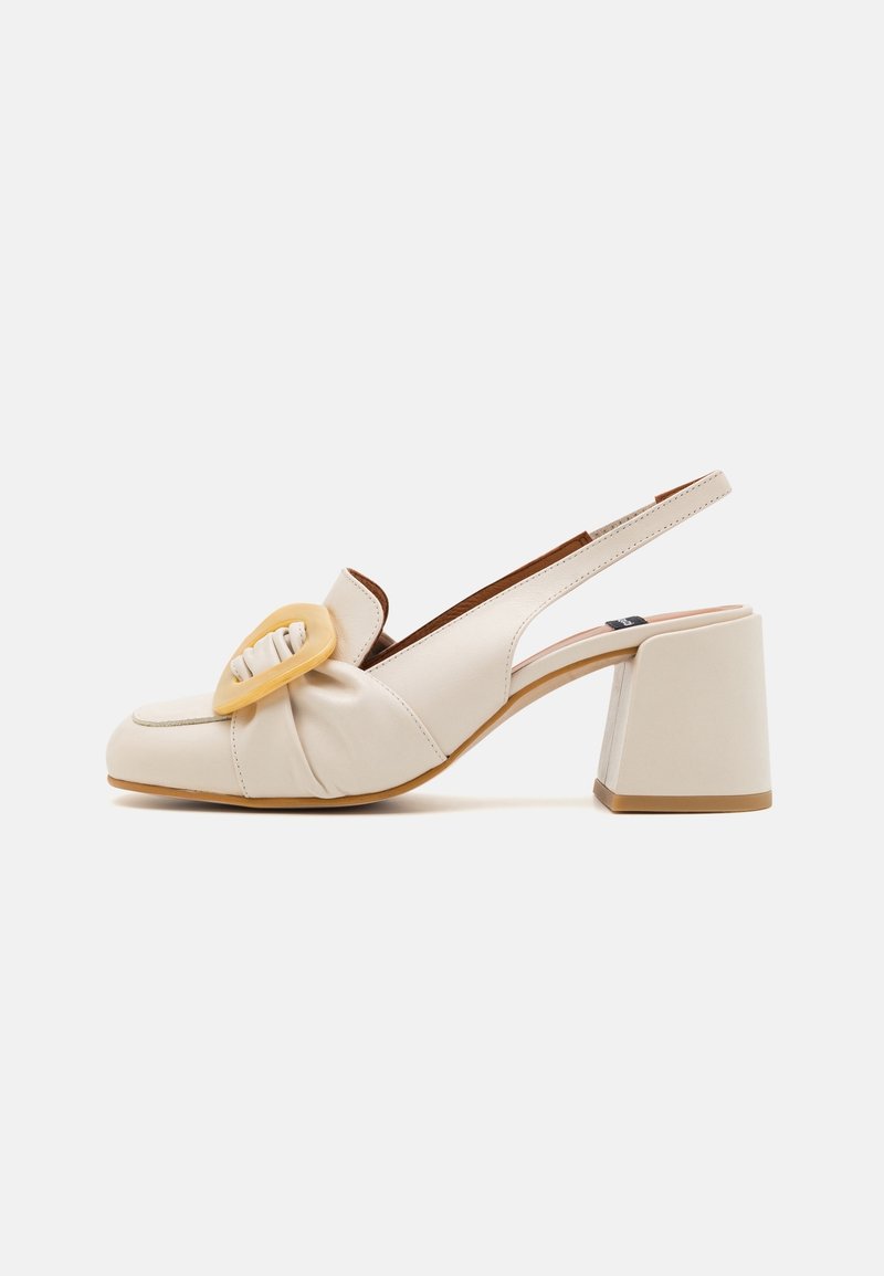 Chaussure slingback en cuir beige avec un talon bloc et une grande boucle décorative à l'avant.